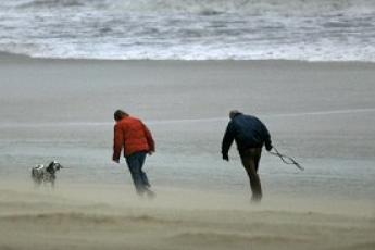 Twee wandelaars trotseren op het strand van Katwijk.