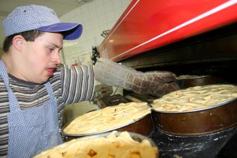 Geconcentreerd schuift Nico, die het syndroom van Down heeft, drie appeltaarten in een oven.