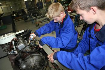 Twee leerlingen van het Wartburg College in Rotterdam sleutelen aan een motorblok.