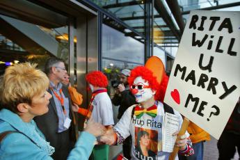 Een demonstrant verkleed als clown in gesprek met een genodigde.