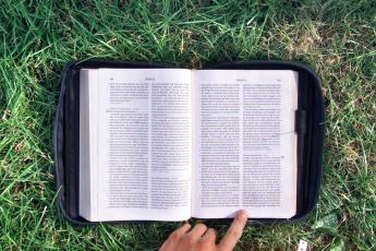 Een jongere leest in het gras uit de Bijbel.